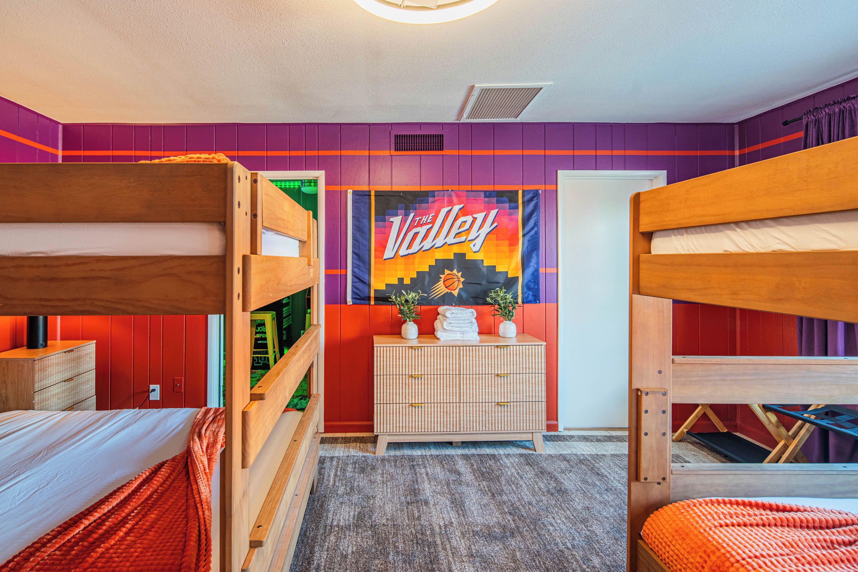A room with bunk beds, a wall-mounted radiator, a door, and a small cabinet with towels and a plant.