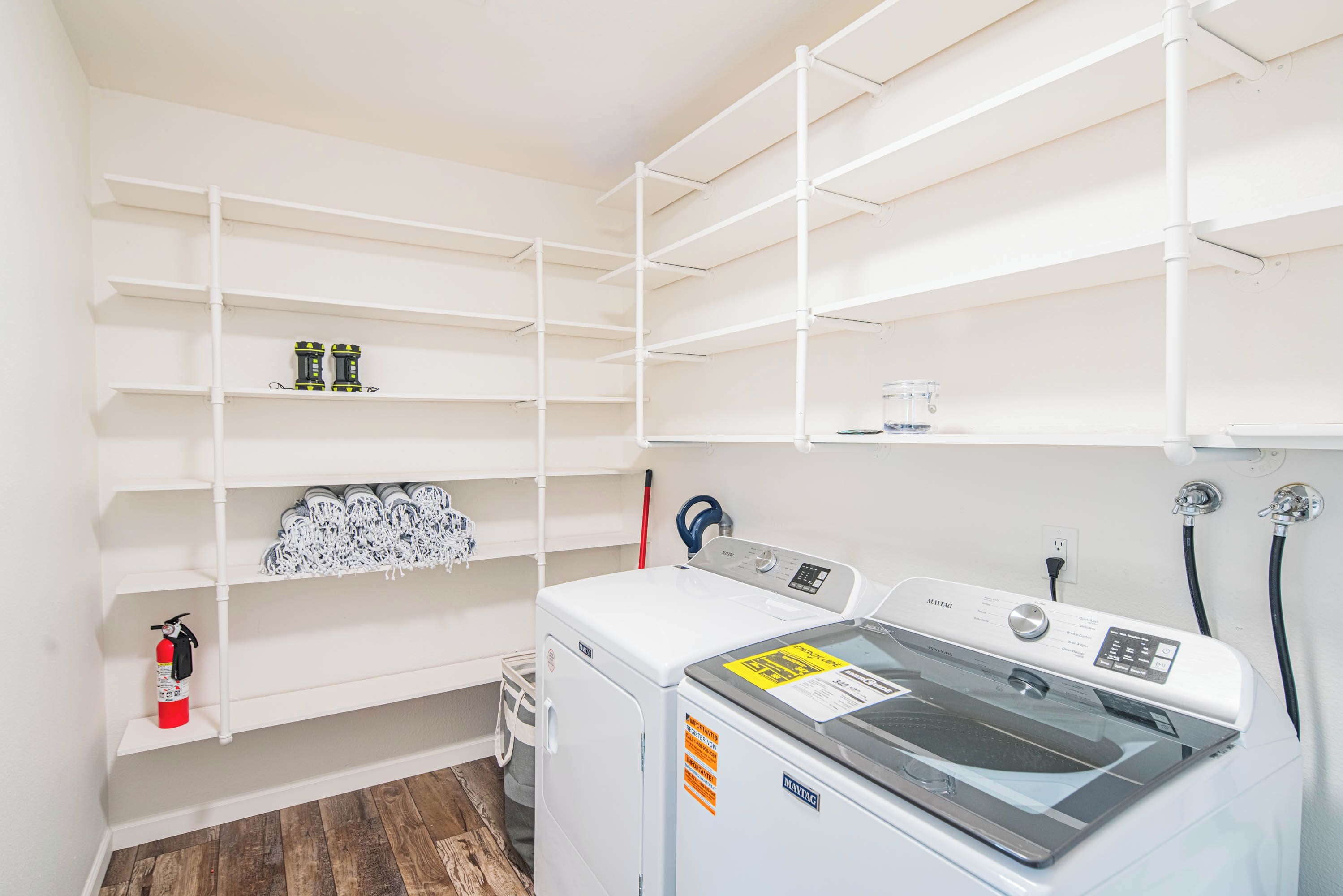 Een wasserij met een voorlader wasmachine, planken met opgevouwen kleding en een brandblusser.