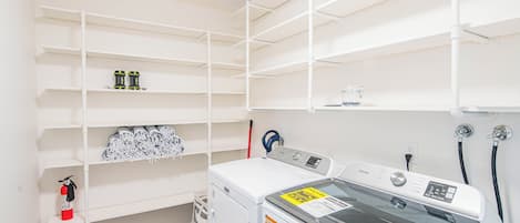 Een wasserij met een voorlader wasmachine, planken met opgevouwen kleding en een brandblusser.