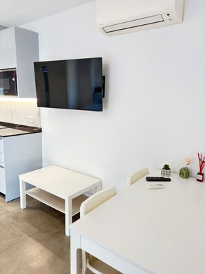 A modern kitchen with a built-in microwave, a flat-screen TV mounted on the wall, a white dining table with chairs, and a small kitchen island. - Short Stay Experts A1 - E1 Studio floor 8 (Gibraltar)