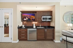 A compact kitchen with a built-in microwave, a stainless steel refrigerator, and a flat-screen TV mounted above the counter. - Luxury Strip View Condo - Balcony - MGM Signature (Las Vegas)