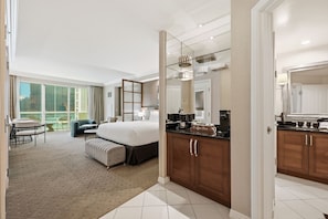 Ein Hotelzimmer mit einem großen Bett, einer Sitzecke mit einer Couch und Sesseln, einer Küchenzeile und Blick ins Freie.