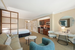 Ein Hotelzimmer mit Bett, einer Sitzecke inklusive Sofa und Sesseln, einem kleinen runden Tisch, einer Küchenzeile mit Mikrowelle und Backofen sowie einem großen Spiegel an der Wand.