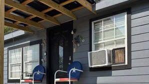 Een houten terras met treden naar een veranda, een brievenbus en een airconditioning aan de zijkant van een huis.