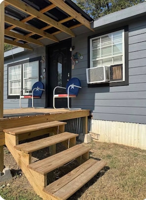 Une terrasse en bois avec des marches menant à un porche, une boîte aux lettres et un appareil de climatisation sur le côté de la maison.