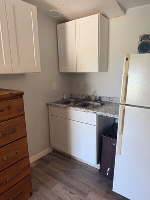 Una cocina con armarios blancos, encimera de granito, pileta de acero inoxidable y refrigerador blanco.