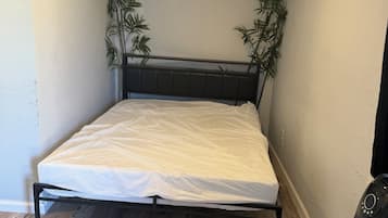 A small, neatly arranged bedroom with a bed, a bedside table, a chair, and two potted plants.