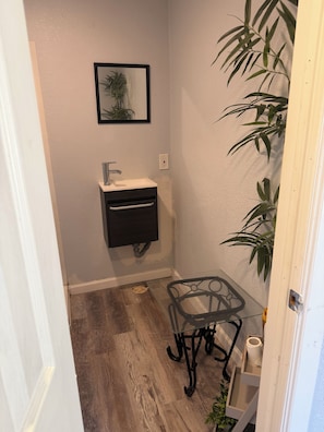 Un baño con lavamanos, espejo y una mesita con una silla.