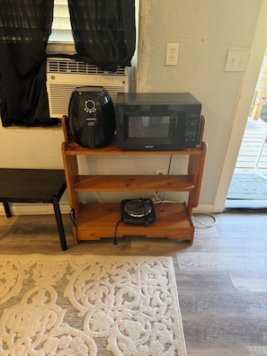 Une pièce avec une étagère en bois sur laquelle sont posés un four à micro-ondes et une machine à café, un banc et un tapis à motifs.