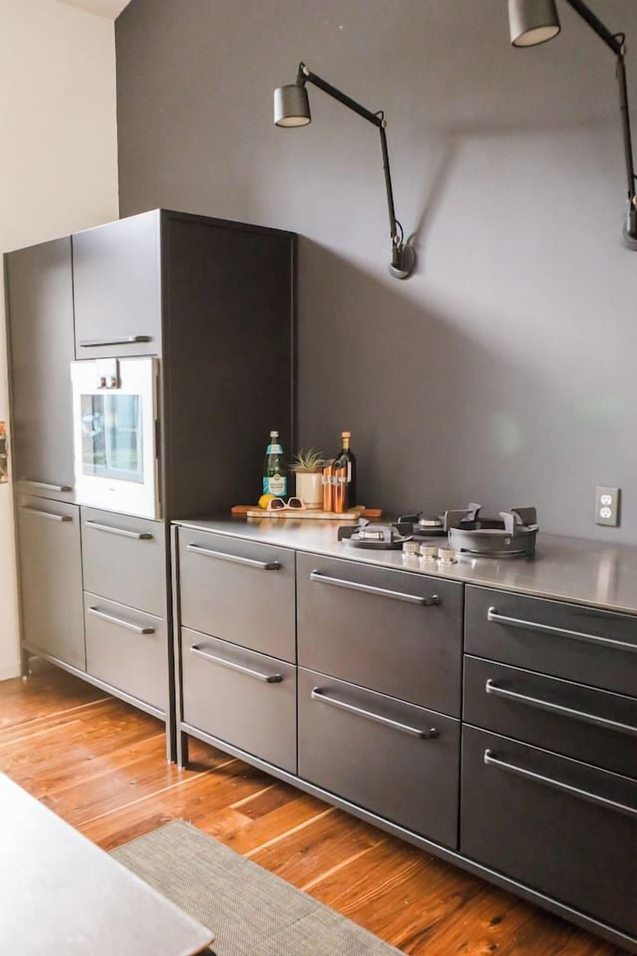 Cozinha moderna com forno embutido, bancada com diversos objetos e luminária fixada na parede.