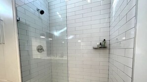 Un baño moderno con azulejos blancos tipo metro, cerramiento de ducha de vidrio y un estante pequeño con artículos de aseo.