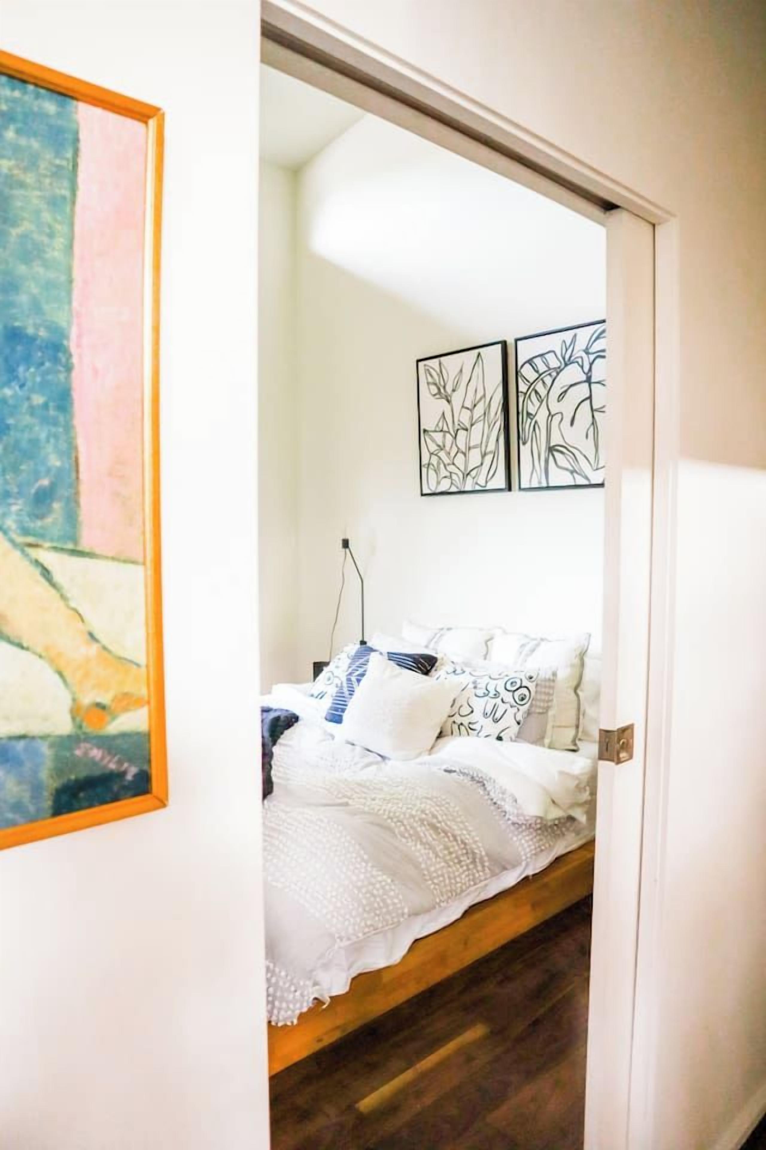 A bedroom with a wooden bed, white bedding, and a painting on the wall.