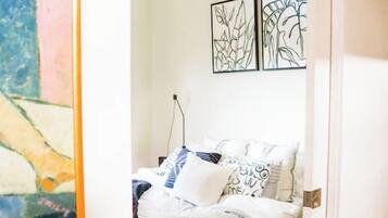 A bedroom with a wooden bed, white bedding, and a painting on the wall.