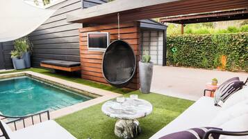 A modern outdoor pool area with a seating arrangement and a hanging chair.