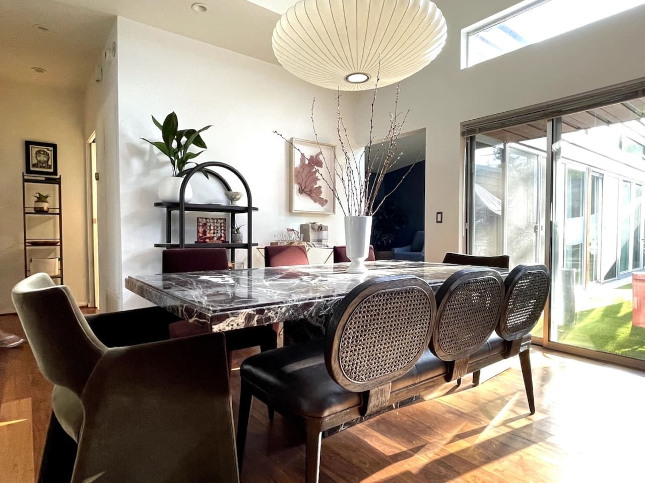 A modern dining area with a marble table, black chairs, and a large window providing a view of the outdoors.