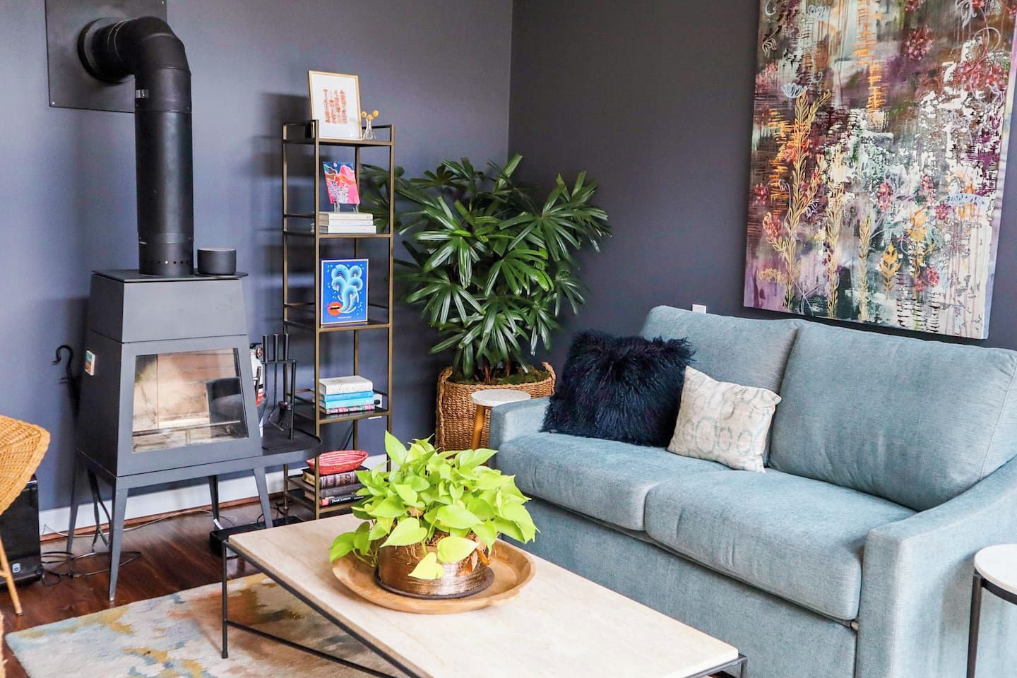 Uma sala de estar com sofá, mesa de centro com uma planta, estante de livros, lareira e um quadro abstrato grande.