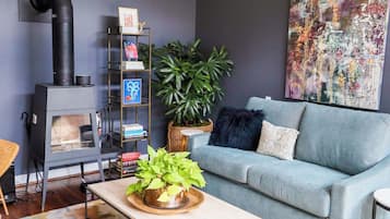Uma sala de estar com sofá, mesa de centro com uma planta, estante de livros, lareira e um quadro abstrato grande.