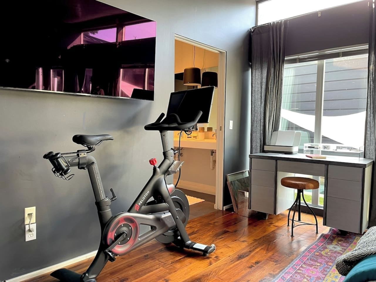 Quarto com bicicleta ergométrica, escrivaninha com computador e janela com cortinas.