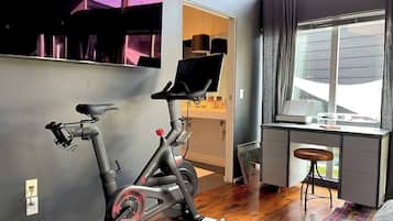 Quarto com bicicleta ergométrica, escrivaninha com computador e janela com cortinas.