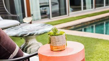 A round table with a potted plant and a glass of orange liquid, likely a cocktail, in a poolside setting.