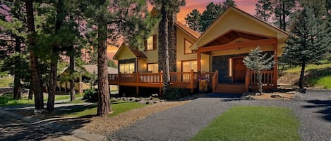 A two-story lodge with a stone facade, wooden deck, and a well-maintained lawn.