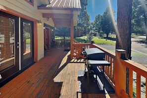A wooden deck with a table and chairs, a covered area with a lantern, and a view of a road and greenery. - Sunny Side Chalet (Ruidoso)