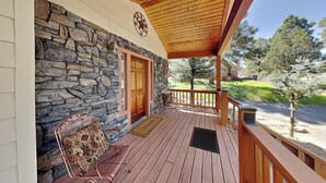 A wooden deck with a stone wall, a wooden door, a metal chair, and a welcome mat. - Sunny Side Chalet (Ruidoso)