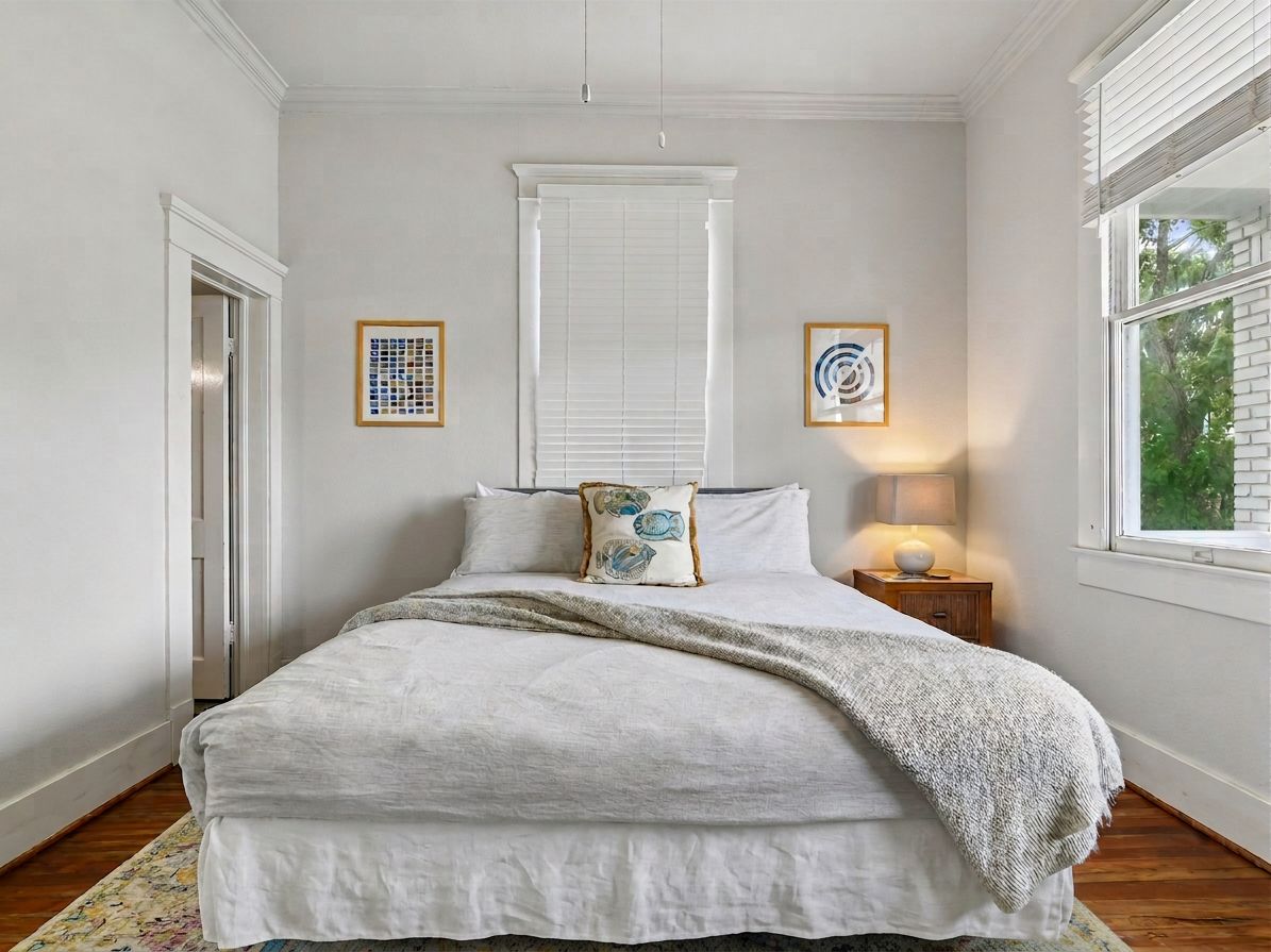Une chambre à coucher comprenant un lit, une table de chevet, une fenêtre et deux œuvres d’art accrochées au mur.