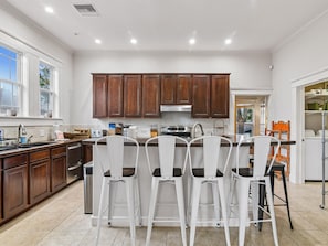 A modern kitchen with white bar stools, wooden cabinets, and a large island. - Galveston Getaway (Galveston)