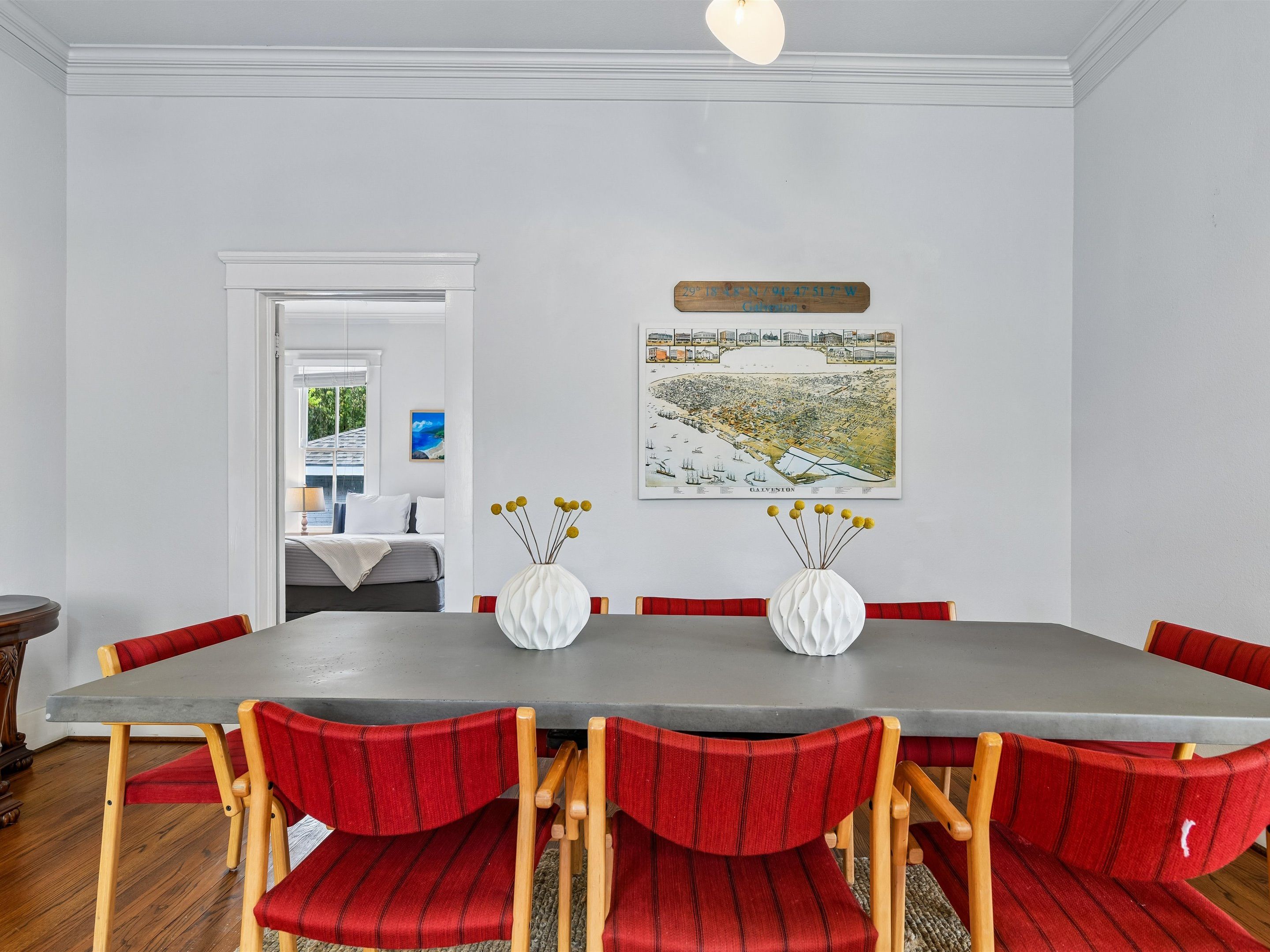 A dining room with a long table, red upholstered chairs, and a white vase with yellow flowers.