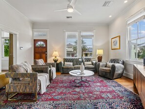 A spacious living room with a large red patterned rug, a ceiling fan, and a view of the outside through large windows. - Galveston Getaway (Galveston)