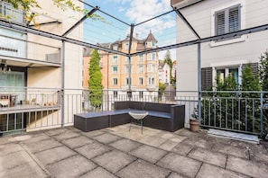 A balcony with a seating area, a potted plant, and a view of neighboring buildings. - Bright 1.5-room apartment in Kreis 6, roof terrace, near ETH (Zürich)
