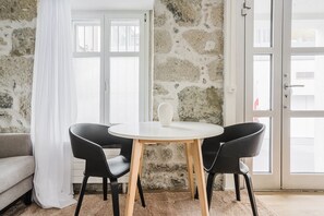 Ein Zimmer mit einer Steinsäule, einer weißen Tür, einem runden Tisch mit zwei Stühlen und einem weißen Sofa.