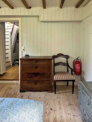 Una habitación con un aparador de madera, una silla con tapicería a rayas, un extintor en la pared y una escalera al fondo.