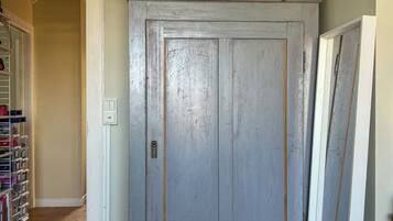 A room with a large grey wardrobe, a wooden floor, and a shelf with decorative items.