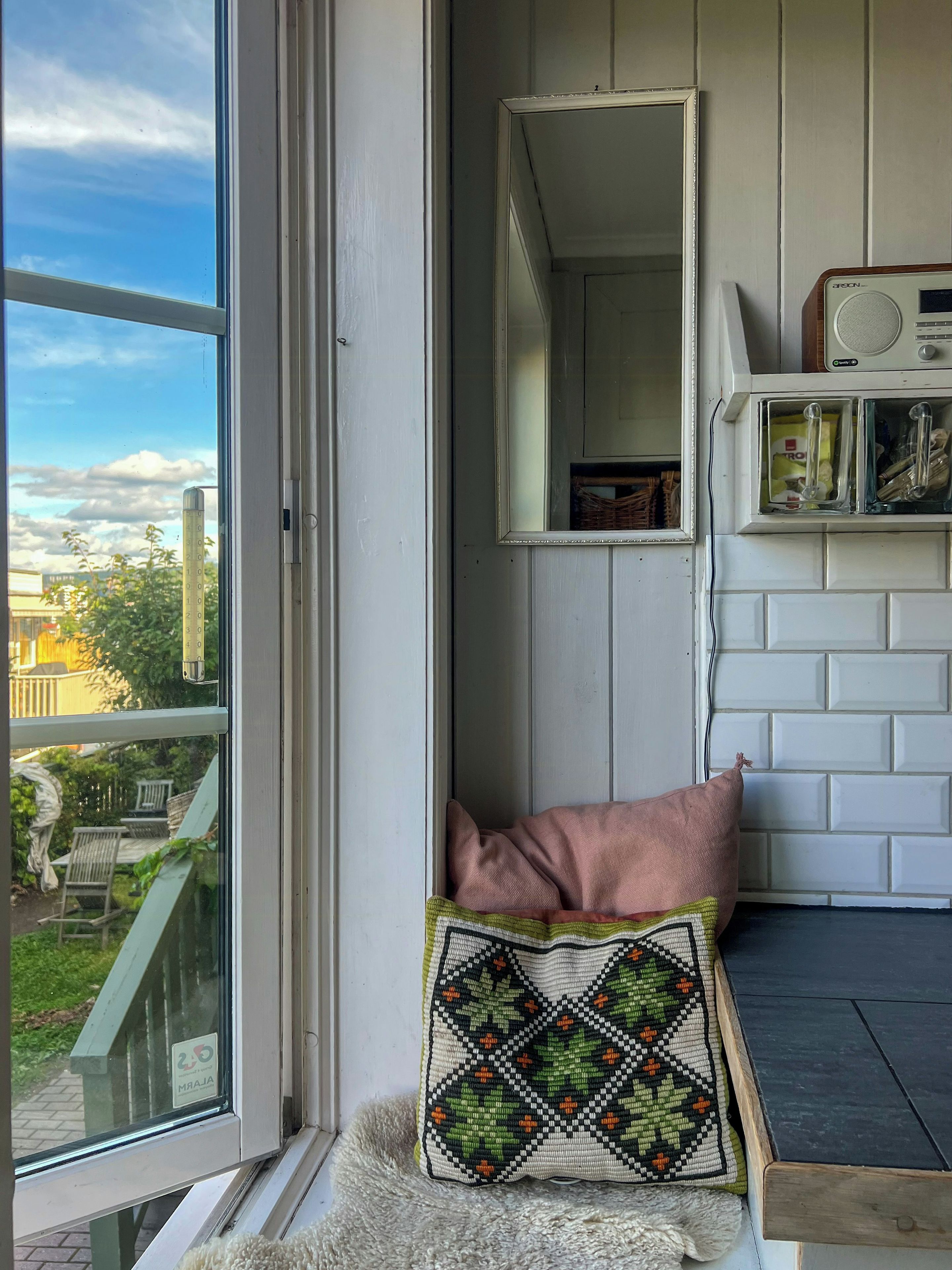 A room with a window, a mirror, a radio, and a cushion.