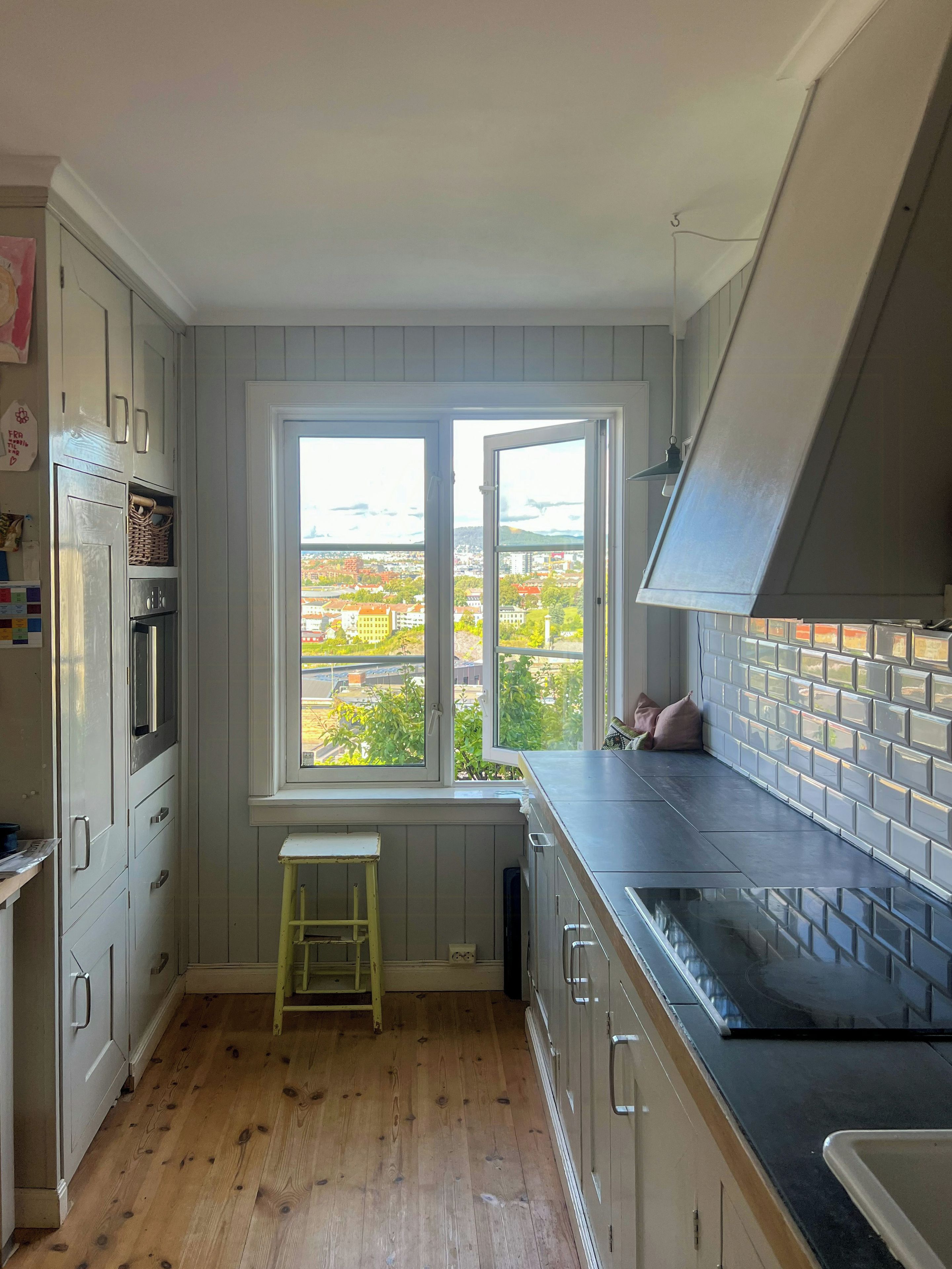 A kitchen with a large window, wooden flooring, and a view of a cityscape.