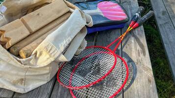 A wooden picnic table with a badminton racket, a blue bag, and a cloth bag with items.