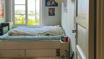 A bedroom with a bed, a window, a door, and a potted plant.
