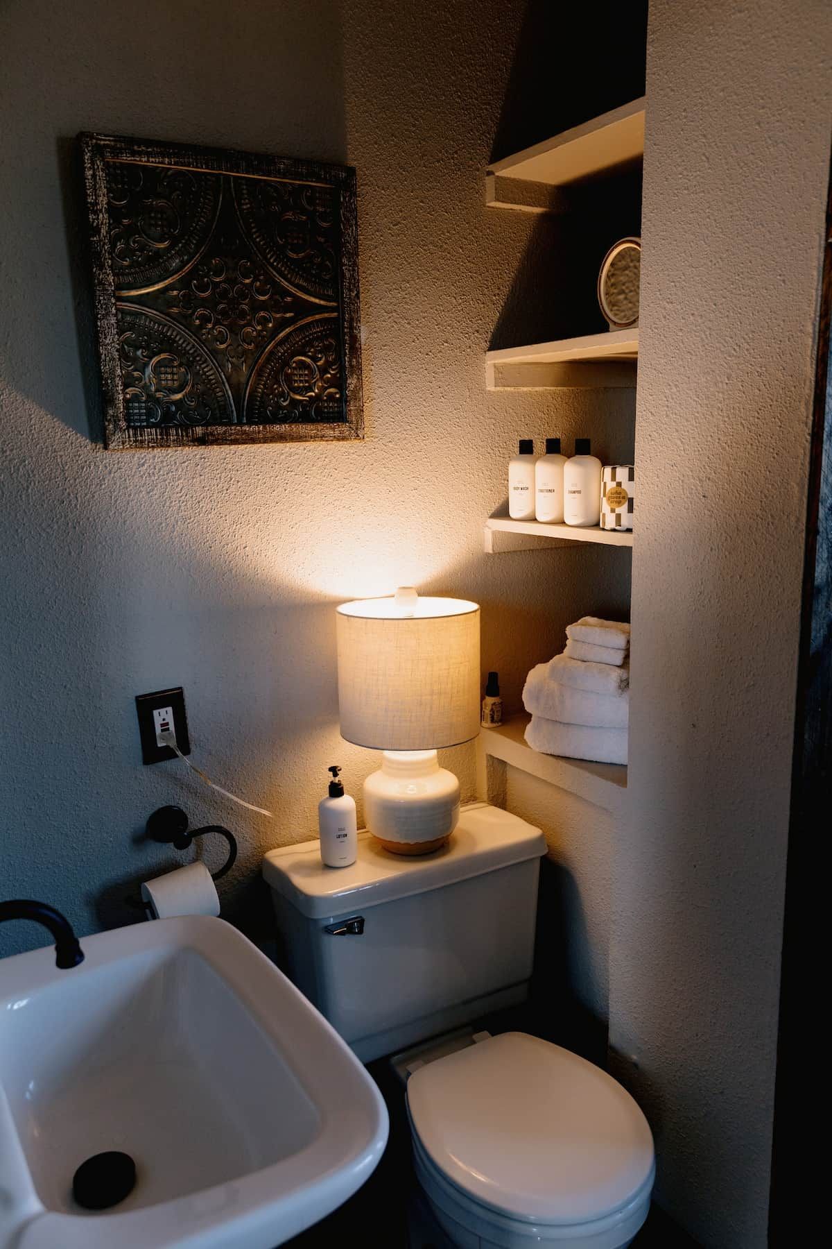 Une salle de bain équipée d’un lavabo, de toilettes et d’une étagère où sont rangés les articles de toilette.