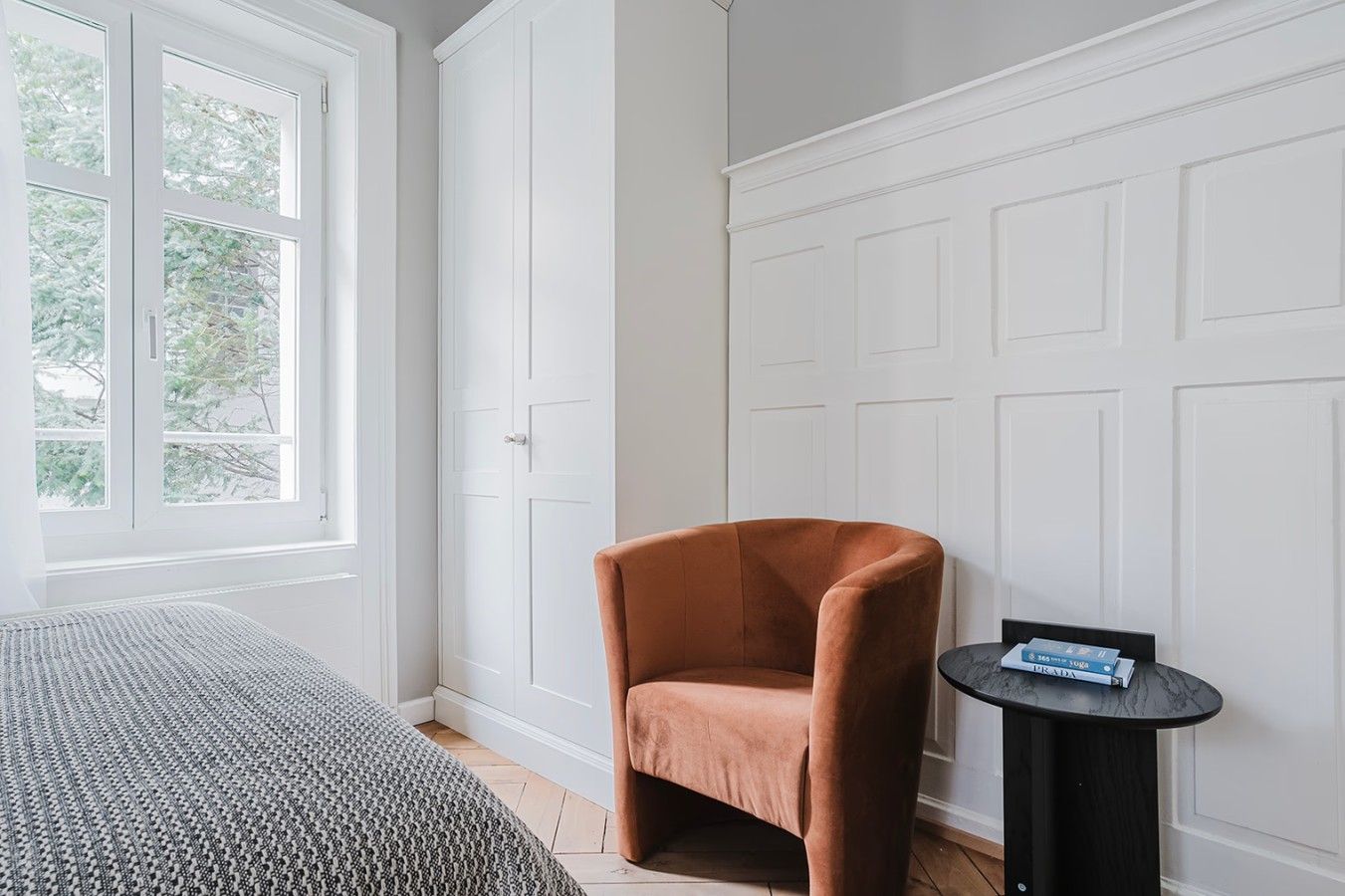 A room with a bed, a chair, and a small table with books.