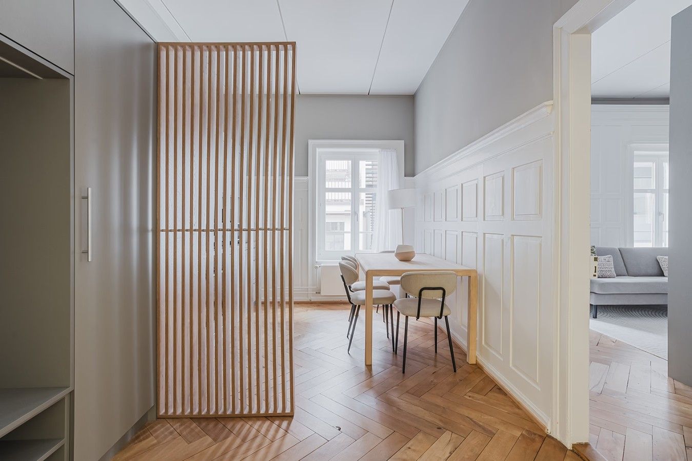 A modern interior with a dining area, wooden floor, and a view into another room.