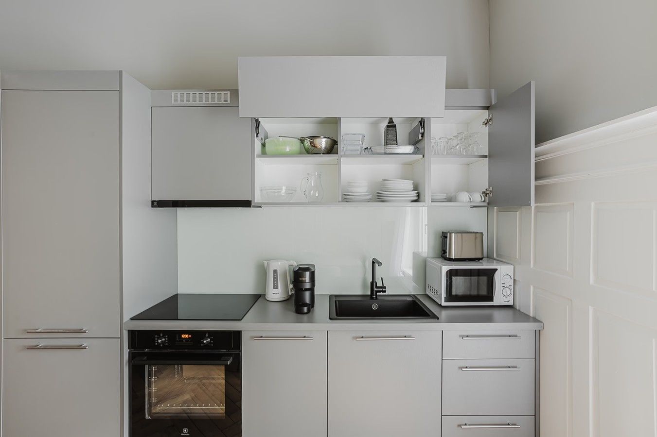A modern kitchen with white cabinetry, a built-in oven, a coffee maker, a microwave, and a sink.
