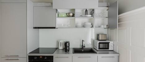 A modern kitchen with white cabinetry, a built-in oven, a coffee maker, a microwave, and a sink.