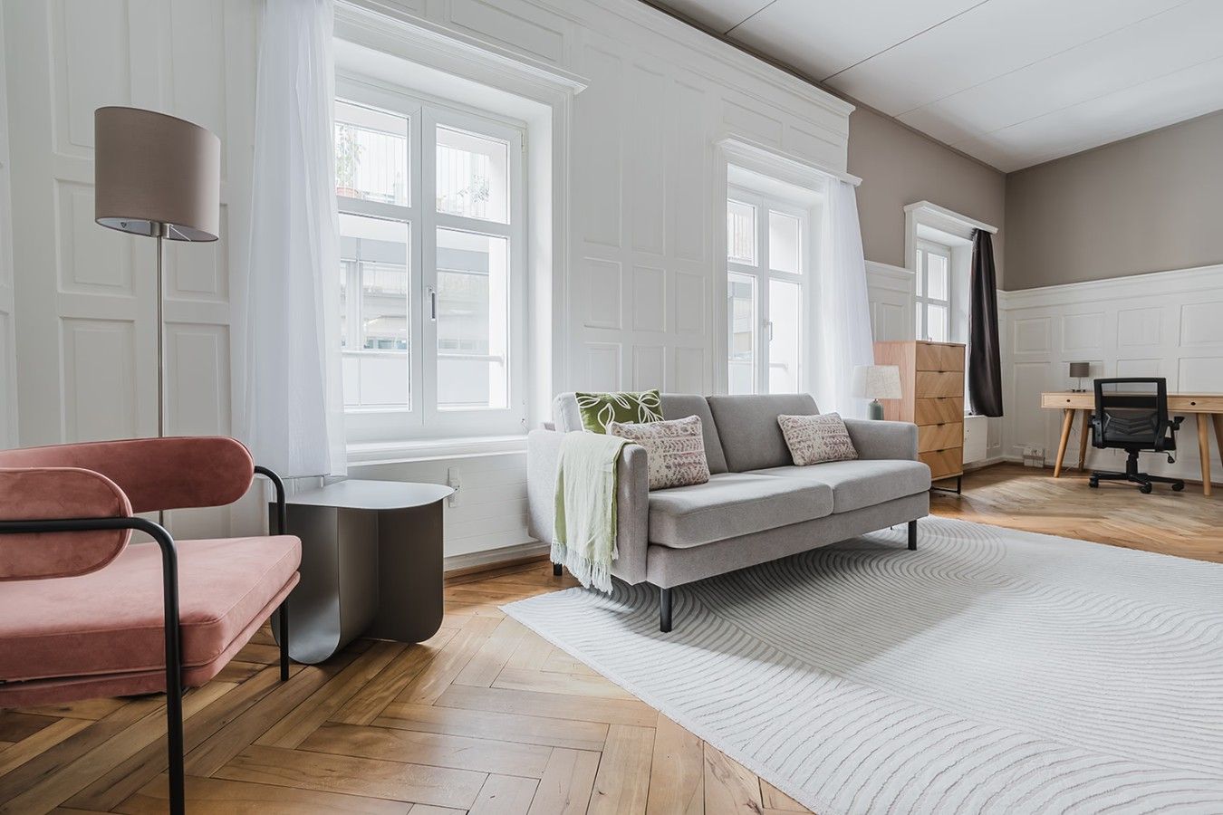 Una sala de estar moderna con un sofá gris, una silla rosa, una lámpara y suelo de madera.