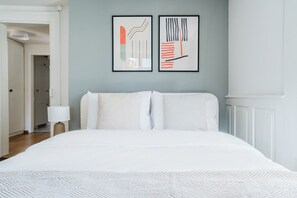 Une chambre d’hôtel avec un grand lit, deux œuvres d’art abstraites encadrées au mur et une table de chevet avec une lampe.