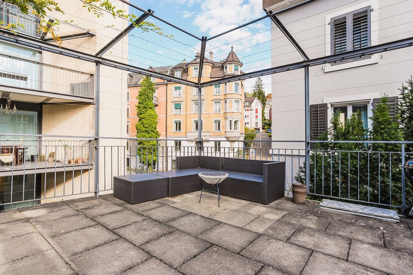A balcony with a seating area, a potted plant, and a view of neighboring buildings.