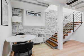 A modern interior with a round dining table, a single chair, a stone wall, a staircase with wooden steps, and a metal railing. - Bright 1.5-room apartment in Kreis 6, roof terrace, near ETH (Zürich)
