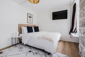 A bedroom with a bed, a bedside table, a lamp, a wall-mounted TV, and a patterned rug. - Bright 1.5-room apartment in Kreis 6, roof terrace, near ETH (Zürich)