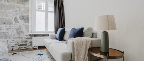 Una sala de estar moderna con pared de piedra, un sofá con cojines, un tapete estampado y una lámpara sobre un pedestal.